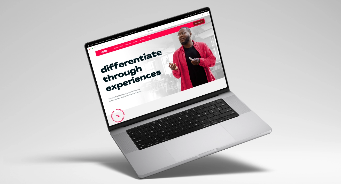 Laptop mit der geöffneten Webseite von shift11, auf der die Startseite angezeigt wird. Ein Mann in einem roten Hemd hält eine Präsentation, während der Slogan "Differentiate through experiences" auf dem Bildschirm zu sehen ist.