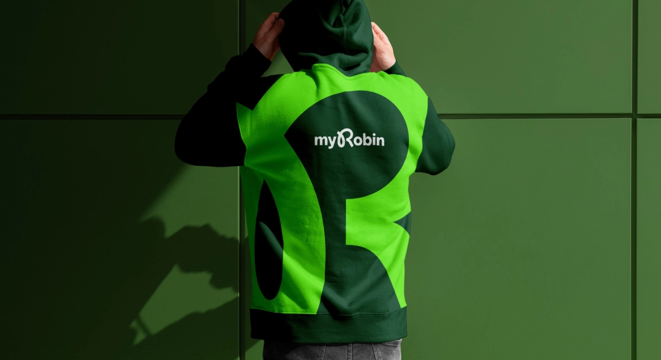 Eine Person trägt einen gebrandeten Hoodie von myRobin. Auf der Rückseite des Hoodies befindet sich das große myRobin-Logo, integriert in ein auffälliges Design in den brandtypischen Grüntönen. Der Hoodie steht im Fokus und hebt die visuelle Identität der Brand hervor.